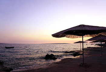 Bamboo sun umbrellas on the empty beach by the sea on the sunset, with pastel color sky and sea