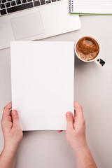 Man's hands holding blank paper on the working desk with computer and coffee