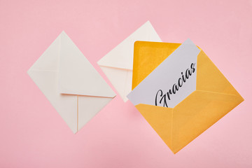yellow bright envelope with gracias lettering on white card near letters on pink background