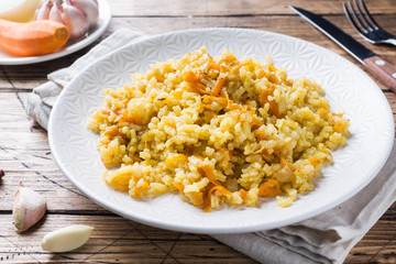 Vegetarian Oriental pilaf with rice and vegetables on a wooden table.