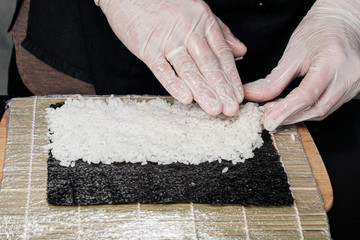 Cook's hands close-up. The chef makes sushi and rolls from rice. White gloves.