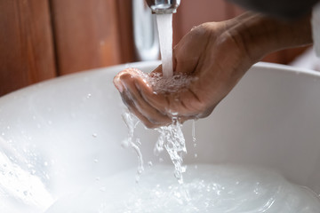 Closeup view african male hand gathering water pouring from faucet