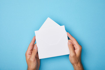 cropped view of man holding envelope with blank white card on blue background - obrazy, fototapety, plakaty