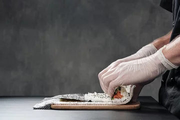 Photo sur Plexiglas Bar à sushi Cook's hands close-up. A male chef makes sushi and rolls from rice, red fish and avocado. White gloves.