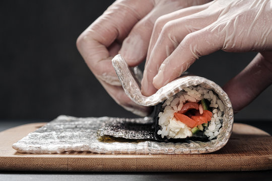 Cook's hands close-up. A male chef makes sushi and rolls from rice, red fish and avocado. White gloves.