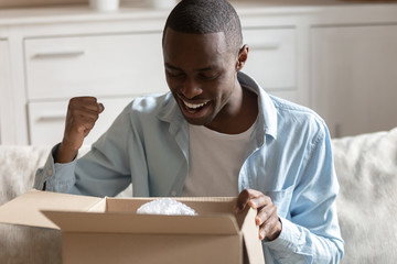 African guy looking inside carton box pleased with received parcel