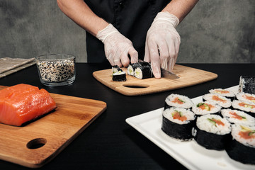 Cook's hands close-up. A male chef makes sushi and rolls from rice, red fish and avocado. White gloves.