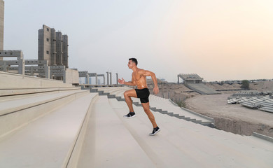 Muscular caucasian male athlete running up a stadium stairs on a hot summer day