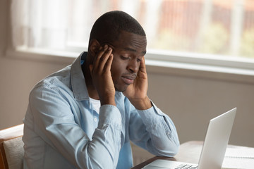 African guy sitting near computer rubbing temples feels unwell