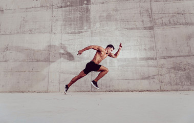 Muscular shirtless caucasian male athlete does an explosive starting sprint against  a grungy...