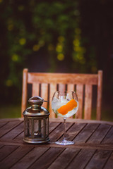 UP OF GIN TONIC AND METAL LAMP ON WOODEN TABLE OF GARDEN