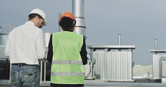 They both turn around and face the site , while the stunning young builder lady points to the landscape and shows the refined construction man the landscape