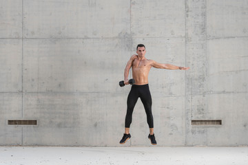 Fototapeta na wymiar Muscular shirtless caucasian male athlete performs a dumbbell weightlifting exercise in a grungy concrete structure while showing his six pack abs 