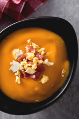 Typical Spanish salmorejo cream with ham and egg on gray background. Top view