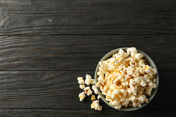 Bowl with popcorn on wooden background, space for text