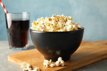 Bowl with popcorn, board and glass with cola on grey background, copy space