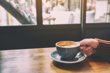 Closeup image of a hand holding a cup of hot coffee on table