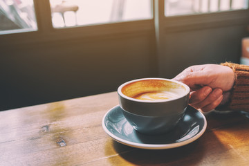 Closeup image of a hand holding a cup of hot coffee on table