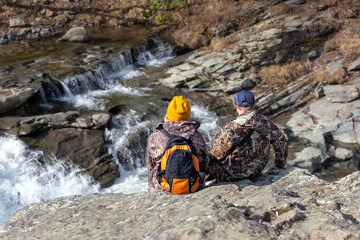Tourists sit on a stone on the Bank of a mountain river