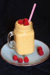 Mango and banana smoothie decorated with raspberries and reusable straw. Selective focus.