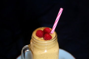 Mango and banana smoothie decorated with raspberries and reusable straw. Selective focus.