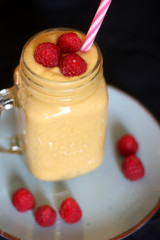 Mango and banana smoothie decorated with raspberries and reusable straw. Selective focus.