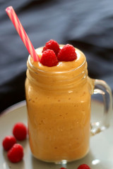 Mango and banana smoothie decorated with raspberries and reusable straw. Selective focus.