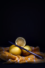  YELLOW LEMONS ON KITCHEN CLOTH AND METAL KNIFE ON DARK BACKGROUND