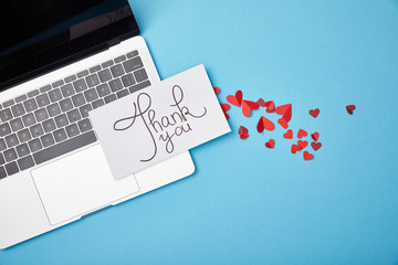 top view of laptop and card with thank you lettering and paper hearts on blue background