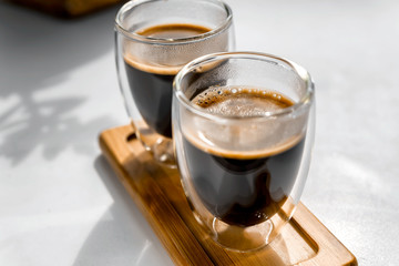 Two cups of fresh espresso on a wooden tray, on a white background. Sunlight from the window