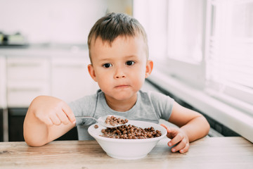 cute baby eating chocolate milk balls in the kitchen in the afternoon