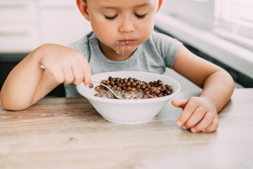 cute baby eating chocolate milk balls in the kitchen in the afternoon