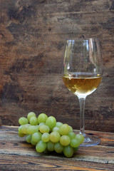 A glass of white wine with grapes on an old wooden background.