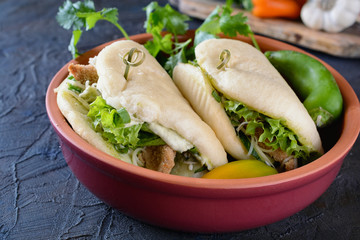 Chinese steam bun, sandwich stuffed with green salad, vegetables and pieces of fried meat in a ceramic bowl on a concrete table, close up