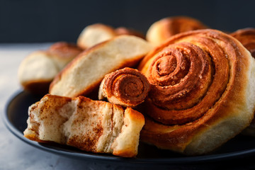 Handmade rolls with cinnamon on a dark dish and on a gray background.