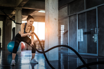 Fototapeta na wymiar Young asian girl training with battle rope in cross fit gym, Battle ropes session.Strong asian woman exercising with battle ropes at the gym with male trainer.