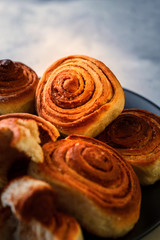 Handmade rolls with cinnamon on a dark dish and on a gray background.