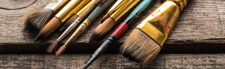 close up view of old paintbrushes on wooden brown surface, panoramic shot