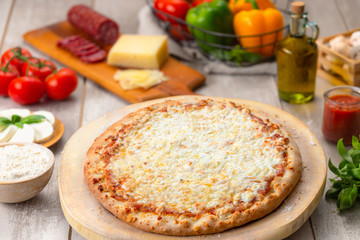 Delicious cheesy whole baked pizza pie with extra cheese, with ingredients on table