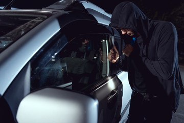 thief intruding car with flashlight and crowbar at night