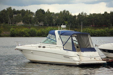 Beautiful white modern inboard motor boat with blue awning at the pier on the river on the background of the old town