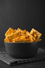 Black bowl with crackers on a dark concrete background