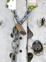 A padlock and iron chains lock an old rusty gate. Safety and strength.