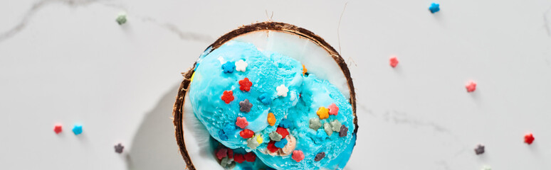 top view of delicious blue ice cream with sprinkles on coconut half on marble grey background,...