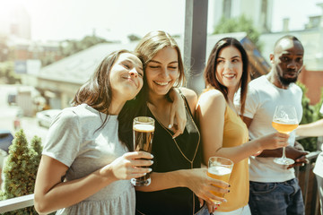 Young group of friends drinking beer, having fun, laughting and celebrating together. Women and men with beer's glasses in sunny day. Oktoberfest, friendship, togetherness, happiness, summer concept.