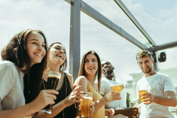 Young group of friends drinking beer, having fun, laughting and celebrating together. Women and men with beer's glasses in sunny day. Oktoberfest, friendship, togetherness, happiness, summer concept.