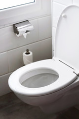 white hanging toilet seat in the hotel home bathroom with white tiles and toilet paper on the wall. Bathroom luxury interior 