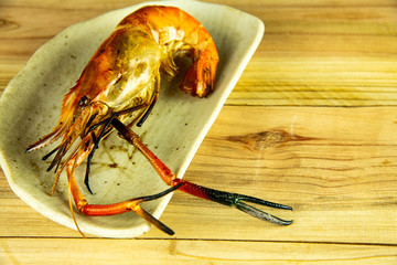 Delicious fresh jumbo grilled shrimps ( head on ), most popular Thai seafood on white dish isolated on wooden background. © Jack Tamrong