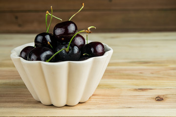 Beautiful sweet ripe cherries in white container bright wooden background.