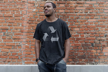 Obraz premium Young attractive man in t-shirt with recycle symbol on brick background. Eco symbol.